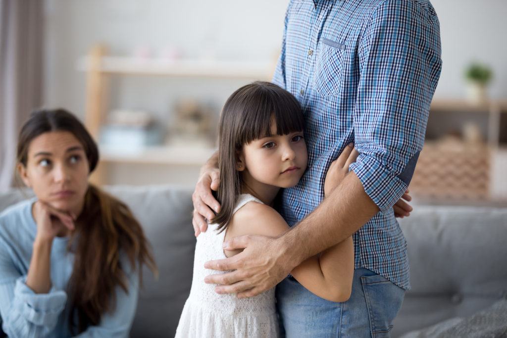 Young girl hugs father as mother looks on concerned. They are going through a divorce, and the girl is going to therapy for children of divorce in West Bloomfield, MI. Therapyology offers a children of divorce support group in West Bloomfield, MI.