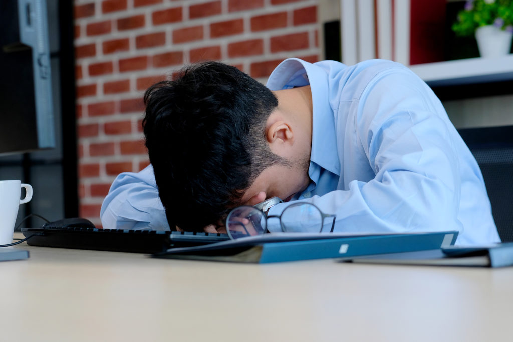 A man hides his face by laying his head on his desk. This could symbolize the stress of starting a first job. We offer support for young adults adapting to change. Contact us for transitions counseling in West Bloomfield, MI, life transition counseling, and more.