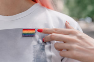 An person points to the pride flag pin on their shirt. This could represent LGBTQ youth support in West Bloomfield, MI. The Rainbow Group was created as support for LGBTQ youth. Learn more about an online LGBTQ support group today!