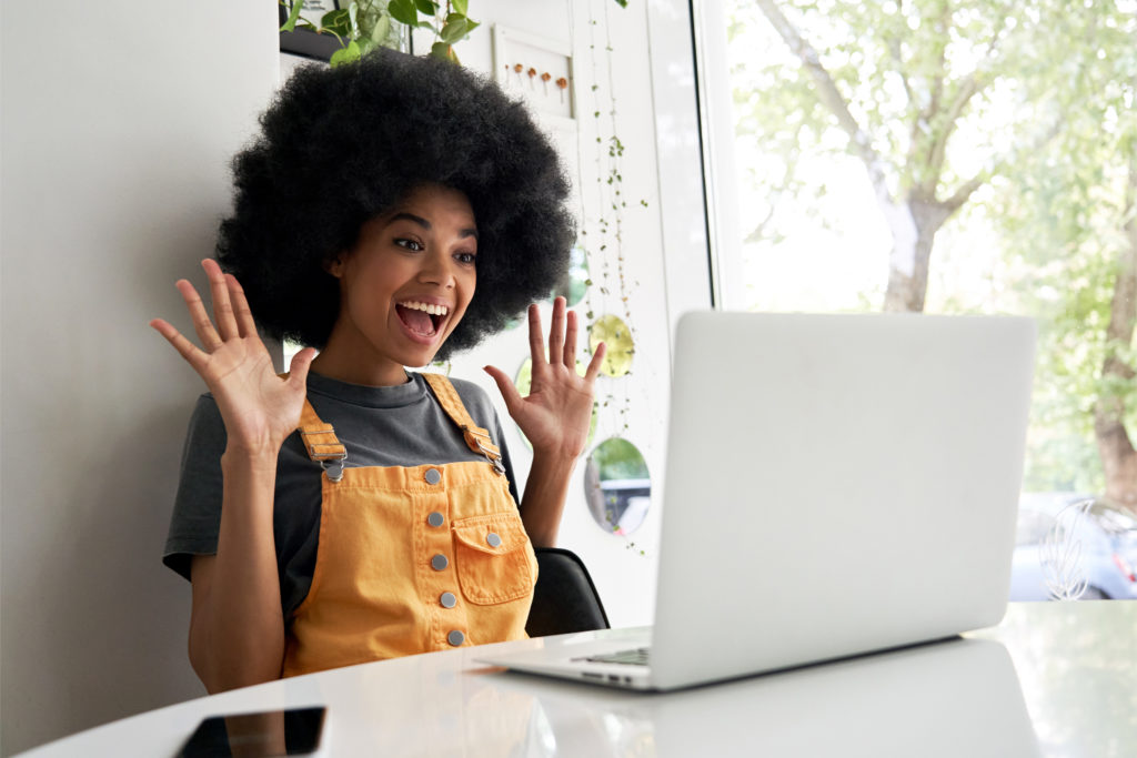 A woman waves both hands as she smiles at her laptop. This could represent online therapy in Michigan, and the benefits that come from meeting with an online therapist in Michigan. Contact us to learn more about online therapy for teens and other services!