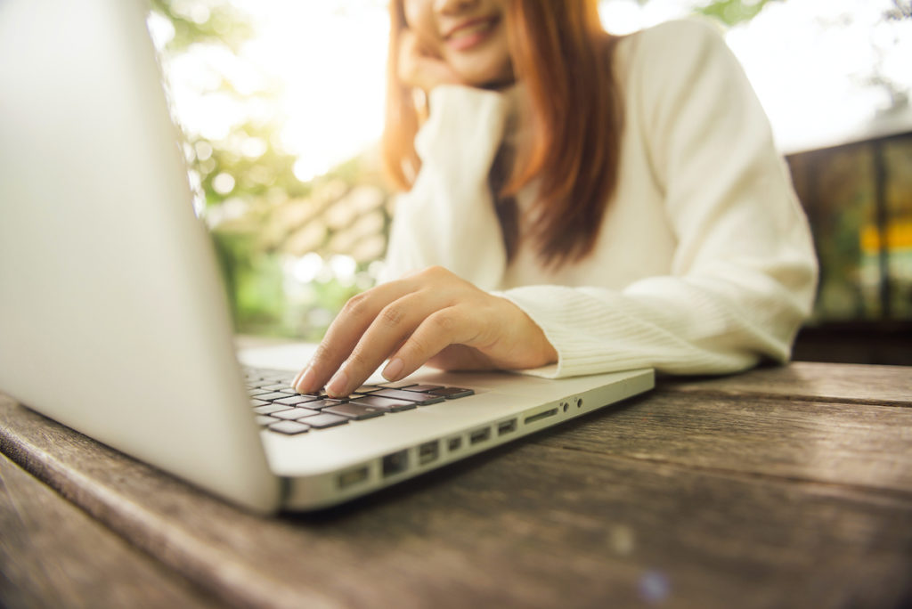 A woman smiles as she types alone on her laptop. This could represent the privacy that comes from online therapy in Michigan. An online therapist can support you with online therapy for teens and a variety of services.