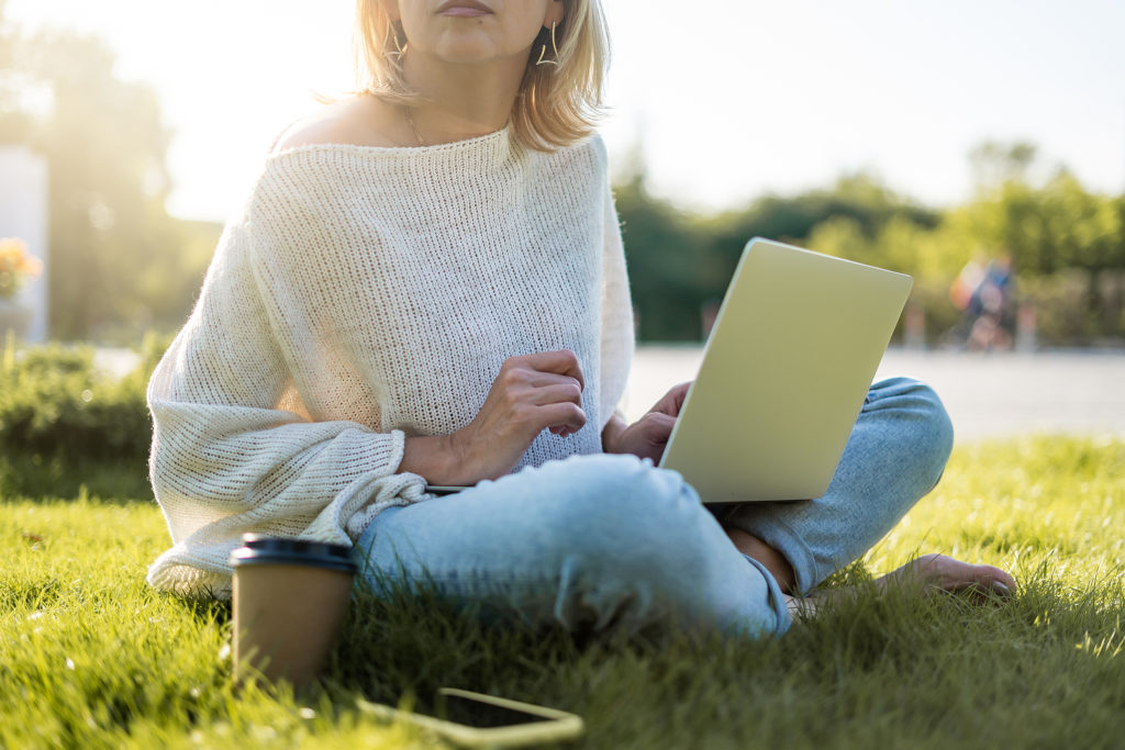 A woman sits in the grass wtih a laptop and coffee nearby. This could represent the convienence of online therapy in California. Learn more about online trauma therapy and other services from an online therapist in California