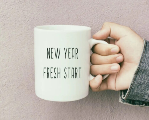 An image of a hand holding a mug with the words " new year fresh start" on the side for Therapyology. We offer life transitions counseling in Michigan, and California. Contact us to learn more about life transitions counseling in West Bloomfield, MI today!