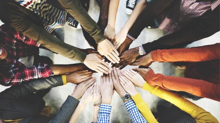 A top down view of a group of people putting their hands into a pile for Therapyology. This represents the support group therapy in West Bloomfield, MI can offer. Learn more about group therapy in San Francisco, CA, and the services we offer including group therapy for teens, trauma group therapy, and more! | 48322 | 94118 | 48324