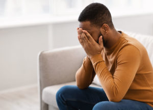 A man covers his face as he sits on a sofa. He appears to be suffering from anxiety. Contact an online therapist in Michigan to learn how a young adult therapist in West Bloomfield, MI can offer support. Or, learn more about options for online therapy in California today! 94118 | 48322 | 48323