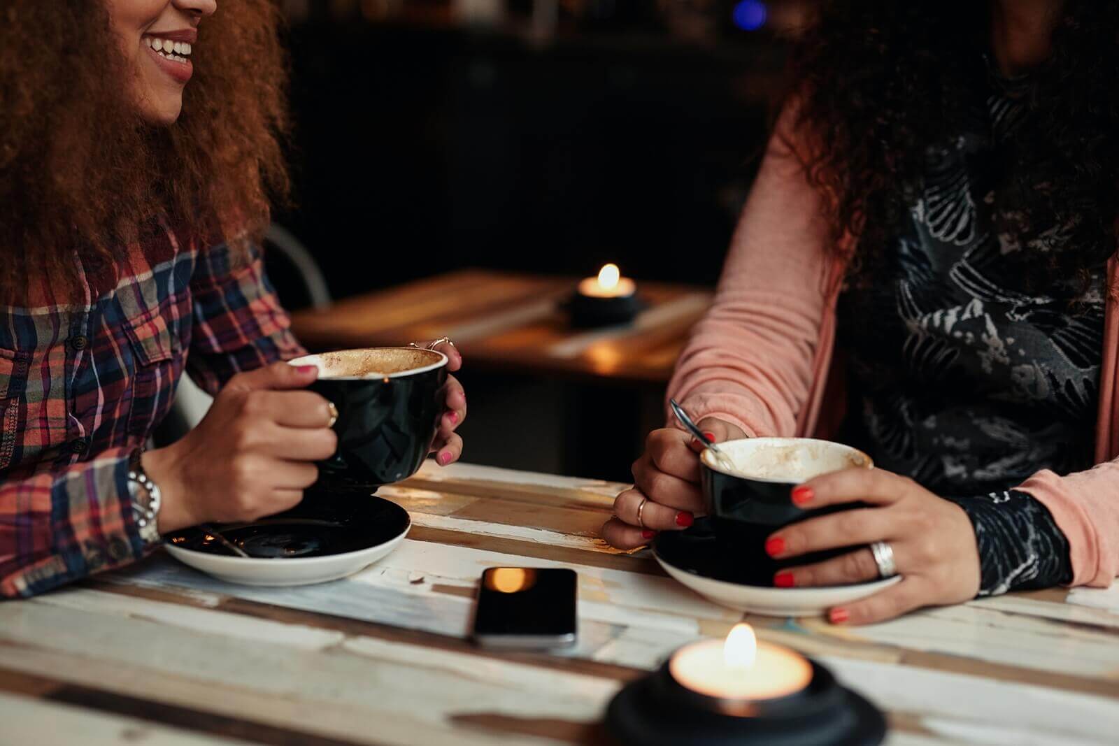 Image of two women sitting at a table drinking coffee and laughing. Learn what your friendship means to you and how to maintain that connection with young adult therapy in West Bloomfield, MI. Find support from a skilled therapist.
