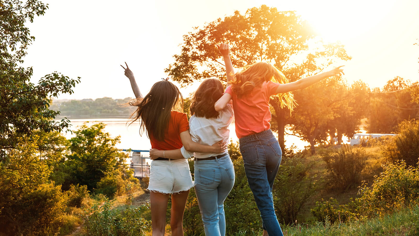 Image of three woman hugging and walking toward a lake while the sun sets. This image represents the importance of friendships and what they can mean to your life. Find support maintaining your connections with a skilled young adult therapist in West Bloomfield, MI.